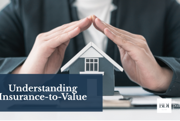 Hands forming a protective roof over a miniature house model on a desk, symbolizing property insurance coverage.