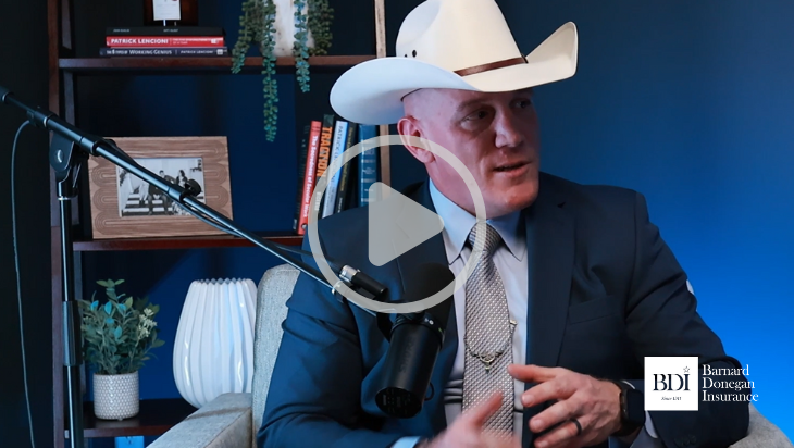 Sheriff Joshua Ray discussing human trafficking awareness for hotel owners in a professional setting, featuring a microphone and a video play button.